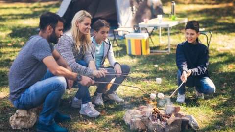 group of people roasting marshmallows next to their tent