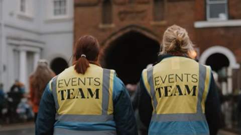 The back of two people walking towards North Bar, wearing hi vis jackets reading 'Events Team' on the back.