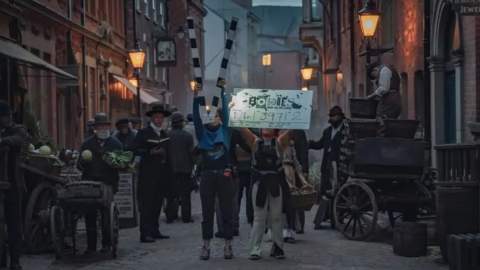 Set of High Street in Hull for Bodies TV show. Actors stand in costumes whilst set assistants hold up boards.