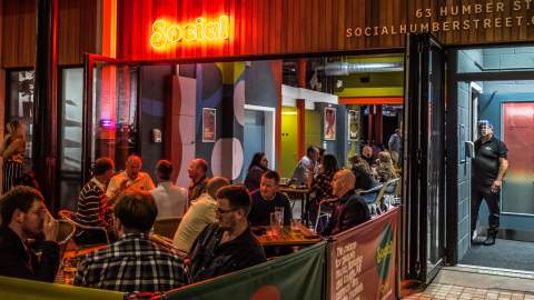 Evening scene at Social on Humber Street in Hull, with people enjoying outdoor drinks and dining under neon lighting, creating a lively atmosphere in the Fruit Market area