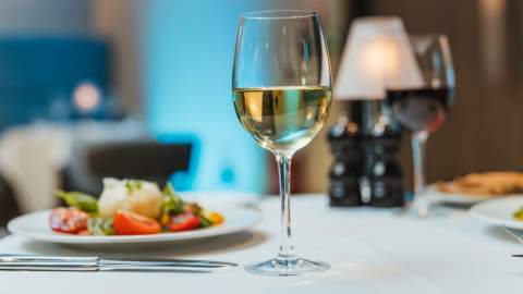 A close‑up of Marco Pierre Whites table setting in Hull with a glass of white wine, plated fine‑dining dishes and soft ambient lighting creating an elegant dining atmosphere.