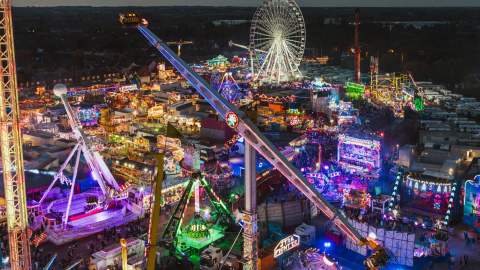 Aerial night view of Hull Fair with bright lights, large rides, food stalls and the illuminated Ferris wheel creating a vibrant festival atmosphere.