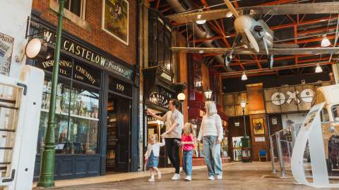 A family of 2 adults and 2 children looking in a museum. A vintage aeroplane is above their heads.