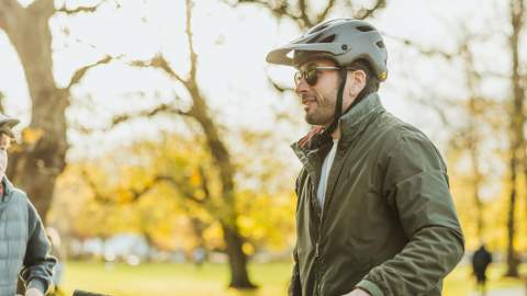 Two cyclists wearing helmets standing with their bikes on a tree‑lined path in Hull’s Pearson Park during autumn