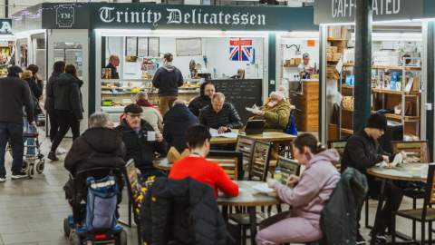 Visitors, including wheelchair users and people with mobility aids, enjoy the accessible indoor food stalls and seating areas at Trinity Market in Hull. The scene highlights step‑free access, spacious walkways, and inclusive dining options within the market