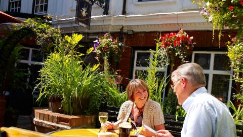 Outdoor courtyard of Ye Olde White Harte pub in Hull, featuring hanging flower baskets, lush plants and visitors dining at a wooden table in a sunny garden setting.