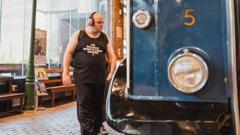 A visitor walking through a transport museum beside a vintage blue bus with the number 5 on the front, surrounded by historic displays and industrial-style interior features.