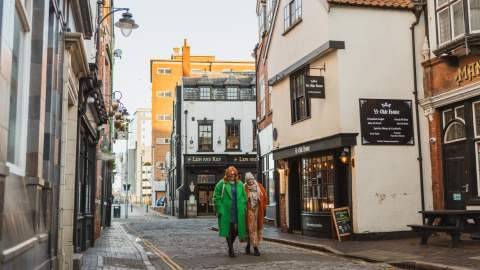 Visitors walking down a historic cobbled street in Hull’s Old Town, passing traditional pubs including Manchester Arms.