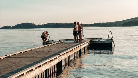 Mennesker som bader fra brygga på Høysand. Foto.