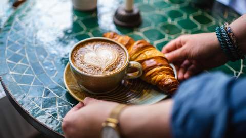 Kaffekopp med hjerteskum og en croissant servert på ett bord