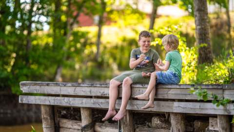 To gutter som sitter på en brygge og leker stein saks papir