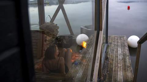 Kvinne sitter i en flytende badstu og ser utover vannet