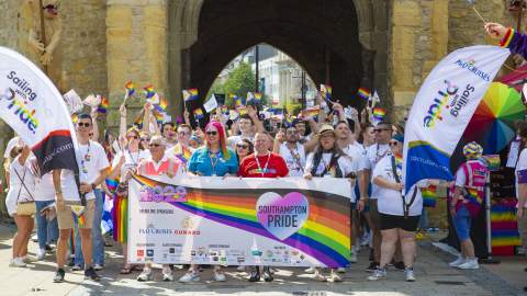 A group of people at the front of the Southampton Pride march in front of the Bargate holding rainbow flags and banners