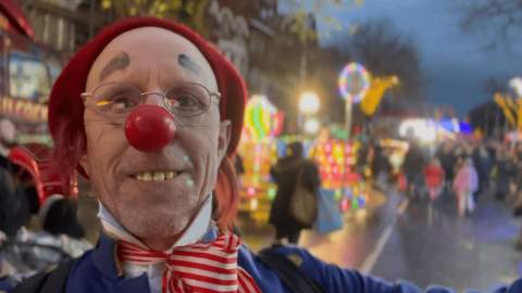 A person dressed as a clown wearing a red nose and a red hat.