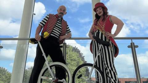 Two people dressed in traditional circus clothes stood holding unicycles.