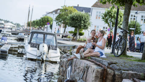 A young family sitting at the harbour edge in Risør, eating ice cream