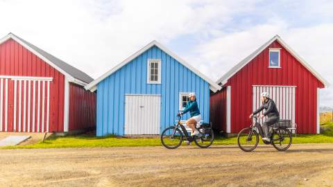 En mann og en kvinne på sykkel foran båthus i Farsund