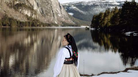 Young lady wearing national costume standing by the river and steep mountains. Photo