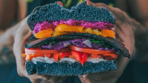 A black burger bun packed full of peppers, cabbage and tomatoes