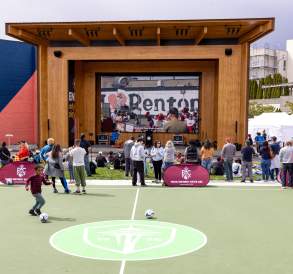 Crowd gathered at Legacy Square in downtown Renton watching a live soccer match on a large outdoor LED screen, with spectators, event activities, and a futsal court in the foreground.