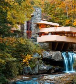 Iconic architectural building Fallingwater sits atop a waterfall with fall foliage surrounding.