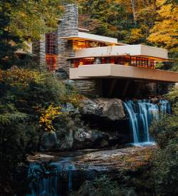 A modern, tan home , known as Frank Lloyd Wright's Fallingwater, situated on top of a waterfall with fall foliage-filled trees surrounding it