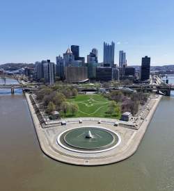 Aerial view two rivers running parallel to a fountain in a park with the city skyline of Pittsburgh