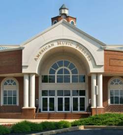 Exterior of a theatre with an arched entrance with windows all along the front entry way. Text on the arched entrance reads American Music Theatre.