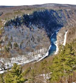 An aerial view of a snowy stream in a gorge with green trees