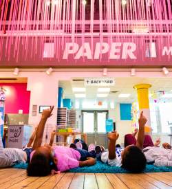 Kids lying on their backs in a classroom pointing up at the ceiling