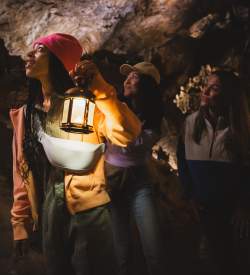 Three women, one with a lamp, exploring a dark, underground cave