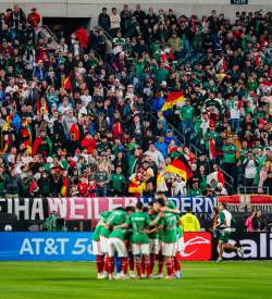 A huddle of soccer players in front of a goal in a crowd-filled stadium