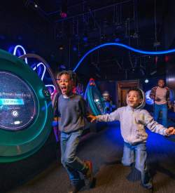 Two kids running around a dark display at the Franklin Institute