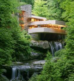 A modern home sitting on top of a waterfall with green trees surrounding it