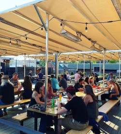 People sit at picnic tables under a large tent enjoying beers