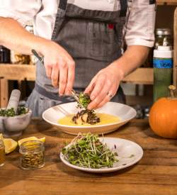 Person in an apron plating a dish with greens