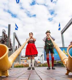 A man and woman in traditional German attire playing large trumpets on a stage