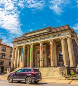 Exterior of the Punxsutawney Weather Discovery Center museum with pillars framing the entrance and cars parked outside the front.