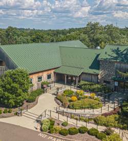Birds eye view of a wooden barn with a green roof and a parking lot in front