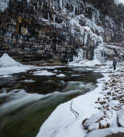A person standing on the banks of an icy river with snow on the ground