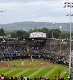 A baseball stadium filled with people watching a baseball game. A sign on the top of the stadium reads Welcome to Howard J. Lamade Stadium