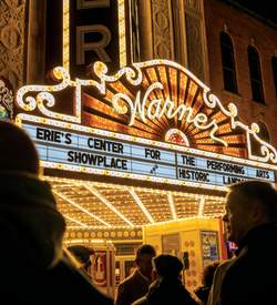 Black silhouettes of people standing in front of a glowing, old school theatre sign that reads Warner Erie's Center for the Performing Arts Showplace