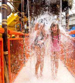 Two young girls getting a bucket of water dumped on them at an indoor waterpark