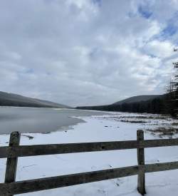 A wooden fence blocking off a frozen lake with snow on the banks