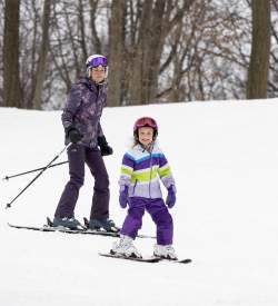 A woman and a small child in snow gear skiing down at hill at Bear Creek Mountain Resort