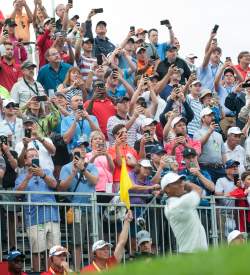 People in stand watching a person hit a golf ball with a club
