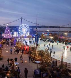 People ice skating at dusk with a large lit up Ferris wheel and Christmas tree and Benjamin Franklin Bridge in the background