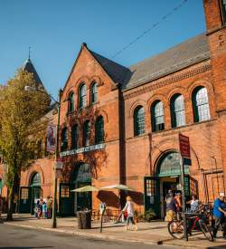 People walk and shop along a street outside a historic red brick building