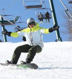 Man in snow gear snowboarding down a snowy hill with a ski lift overhead