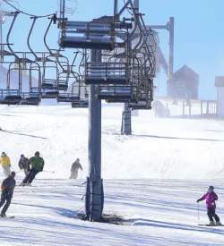 People skiing down a snowy hill with a ski lift above them